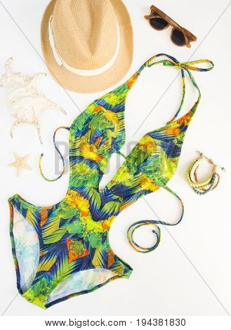 Summer outfit beach outfit summer stuff. Exotic pattern swimsuit wood bracelet retro sunglasses and straw hat. Flat lay top view.