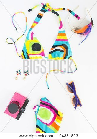 Summer background beach outfit girl summer stuff. Geometric abstract pattern swimsuit pink retro camera bright sunglasses feather headband and earrings. Flat lay top view.