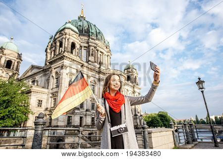 Young woman tourist making selfie with german flag in front of the famous cathedral in Berlin city