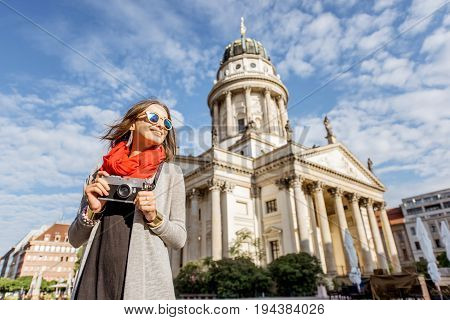 Young woman tourist standing with photo camera on the Gendarmen square with French church and Opera house on the background in Berlin