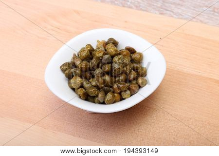bowl with fresh capers on wooden table.