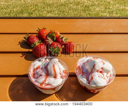strawberries and vanilla ice frozen joghurt cream refreshing cold summer dessert in a takeaway tub on a wooden table