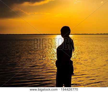 Silhouette of a young woman lit by a sunny path beautiful evening on a liman under a warm sky