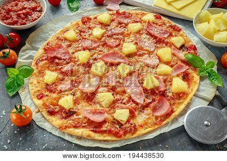 Fresh baked pizza hawaii with ham and pineapple, basil, tomatoes on backed paper.