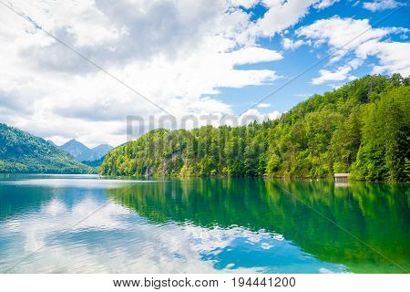 Lake Alpsee near Hohenschwangau castle in Bavaria state with surrounding nature landscape and mountains Germany under cloudy blue sky
