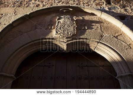 Caceres palace facade. Door with carved shield. Coat of arms Illuminated by last ray of sun