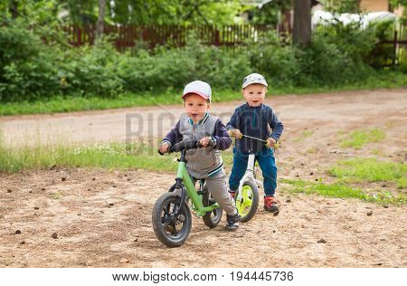 Two happy little boys or toddler 2-3 years outdoors with balance bikes