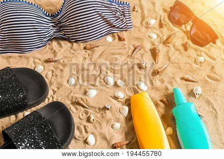 Summer bikini and accessories stylish beach set, Beach bikini summer outfit and sea sand as background, Top View, Concept. Copy space. Sun flare