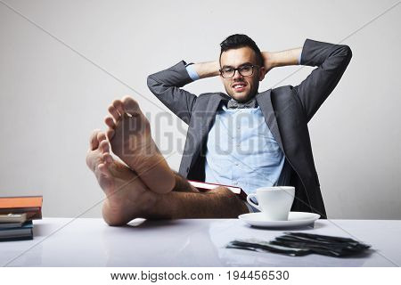 Successful happy young businessman sitting in office with bare feet on desk and relaxing. (Boss business rules officialdom concept)
