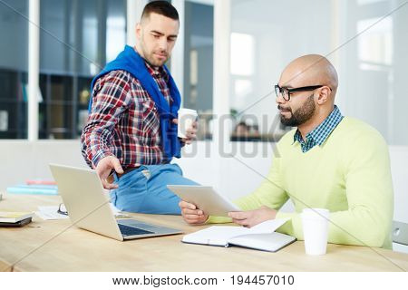 Confient man pointing at laptop display while explaining data to colleague with touchpad