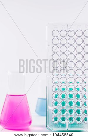 research, science and clinic background. 96 well micro plate and  laboratory beakers with colorful liquids and reagents.