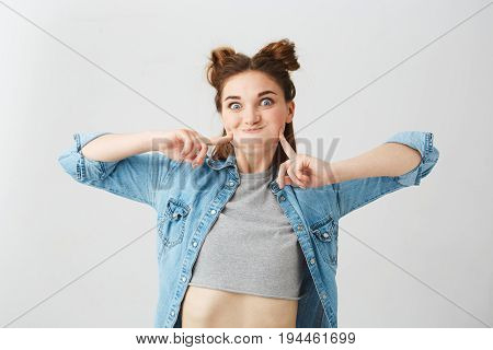 Portrait of funny young pretty girl with two buns making funny face fooling over white background. Copy space.