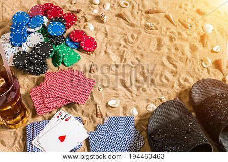 Beachpoker. Chips and cards on the sand. Around the seashells, sunglasses and flip flops. Top view. Copy space. Flat lay. Sun flare