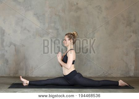Young Woman Practicing Yoga Monkey King Pose, Hanumanasana Against Texturized Wall / Urban Backgroun