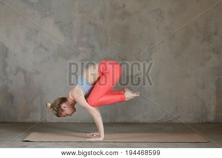 Young Woman Practicing Yoga Crane Pose, Bakasana Against Texturized Wall / Urban Background