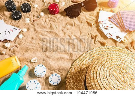 Beachpoker. Chips and cards on the sand. Around the seashells, sunglasses and hat. Top view. Copy space. Flat lay. Sun flare