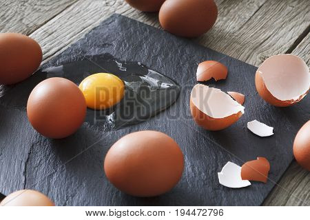Fresh chicken brown home eggs with cracked eggshell and yolk on rustic slate black background. Closeup. Natural healthy food and organic cooking ingredients