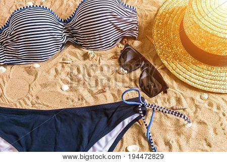 Summer bikini and accessories stylish beach set, Beach bikini summer outfit and sea sand as background, Top View, Concept. Copy space. Sun flare