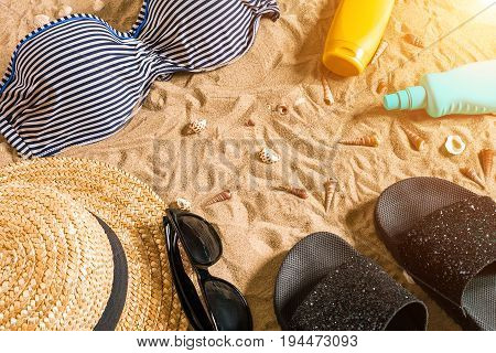 Summer bikini and accessories stylish beach set, Beach bikini summer outfit and sea sand as background, Top View, Concept. Copy space. Sun flare