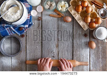 Baking background. Cooking ingredients for dough and pastry making on rustic wood. Rolling pin with unrecognizable hands. Top view with copy space, mockup for menu, recipe or culinary classes.