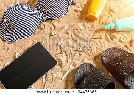 Summer bikini and accessories stylish beach set, Beach bikini summer outfit and sea sand as background, Top View, Concept. Copy space. Sun flare