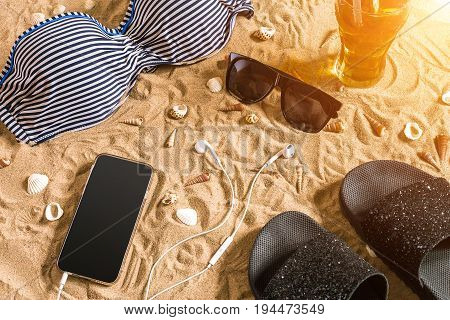Summer bikini and accessories stylish beach set, Beach bikini summer outfit and sea sand as background, Top View, Concept. Copy space. Sun flare
