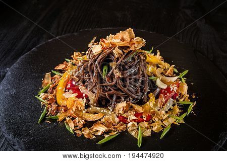 soba noodles of buckwheat Noodles of buckwheat yellow and red pepper, herbs. Pan-Asian cuisine. On stone tray on dark wooden table. Place for text.