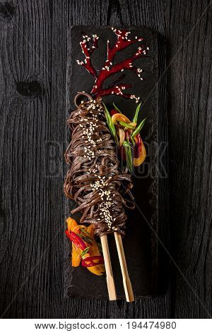 soba noodles of buckwheat Noodles of buckwheat yellow and red pepper, herbs. Pan-Asian cuisine. On stone tray on dark wooden table. Place for text.