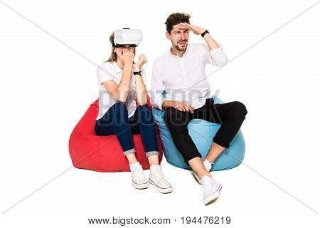 Smiling friends experiencing virtual reality glasses seated on beanbags isolated on white background. Experiencing virtual gaming adventure.