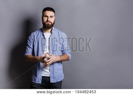 Bearded man with public speaker gesture. Fingers connected at fingertips, pose which imposes power and patience, gray studio background, copy space