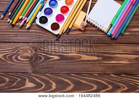 Border from stationery - pencils pen note erazer paint on wooden background. Back to school. Top view. Place for text.