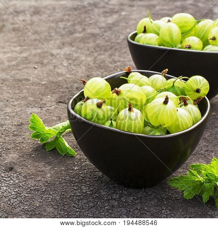 Fresh green gooseberries in a ceramic bowl on a dark background. Top view.