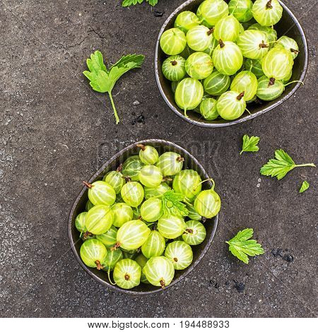 Fresh green gooseberries in a ceramic bowl on a dark background. Top view.