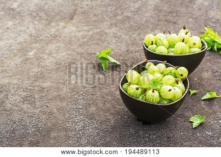 Fresh green gooseberries in a ceramic bowl on a dark background. Top view.