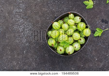 Fresh green gooseberries in a ceramic bowl on a dark background. Top view.