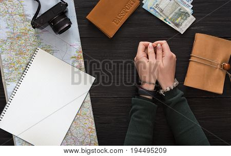Travel background, tourism and wanderlust concept. Top view on dark table with world map, money, passport and other essentials with tourist hands, waiting for vacation, copy space