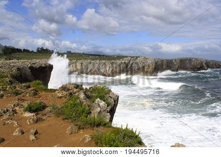 Blue Sky And Waves Splashing Against A Cliff In Pria, Spain