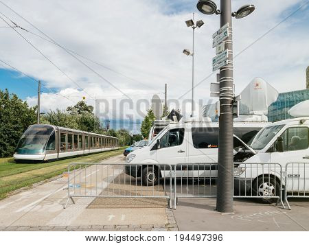 STRASBOURG FRANCE - JUN 30 2017: Tramway passing near TV Media Television Trucks with multiple Satellite parabolic antennas and fiber optic cables preparing to report live the official European Ceremony of Honour for Dr. Helmut Kohl at European Parliament
