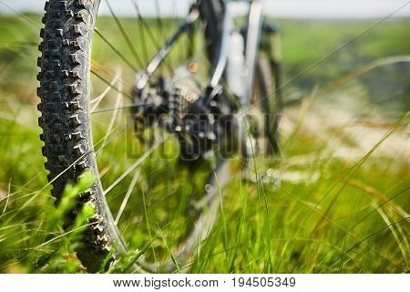 Close-up of the wheel of mountain bicycle in the green grass in the meadow in the countryside. Detail of the mountain bike. Horizontal photo. Sportive backgrounds and still-life. Travel in the countryside. Concept of the healthy lifestyle.