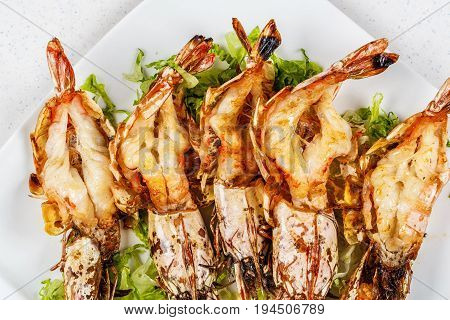 Grilled tiger prawns served with leafs and lemon on white plate.