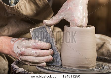 pottery, workshop, ceramics art concept - closeup on male hands sculpt new utensil with a tools and water, man's fingers work with potter wheel and raw fireclay, front close view