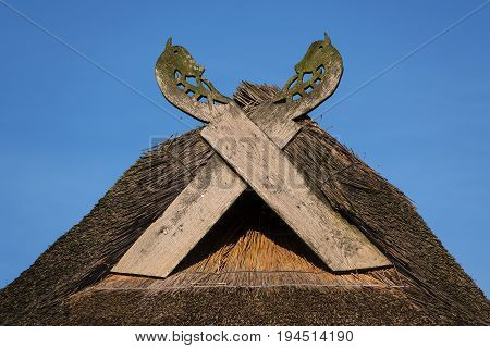 Wooden gabled boards in the form of horse heads on a thatched roof against a blue sky on a sunny day typical of traditional houses in northern Germany