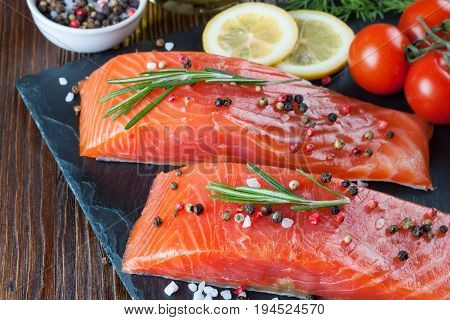 Raw salmon fillet and ingredients for cooking on a slade board and brown wooden background.