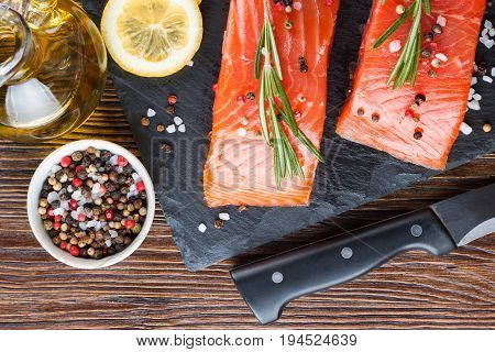 Raw salmon fillet and ingredients for cooking on a slade board and knife on brown wooden background.