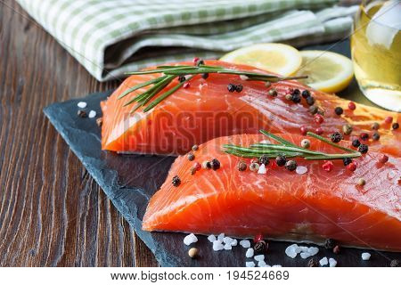 Raw salmon fillet and ingredients for cooking on a slade board and brown wooden background.