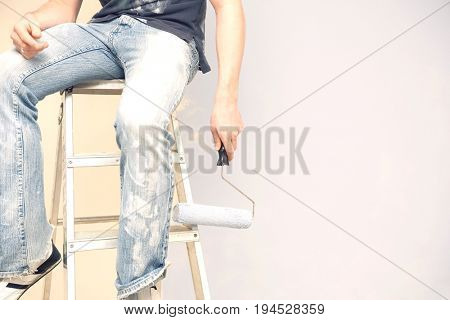 Midsection of man holding paintroller while sitting on stepladder against wall