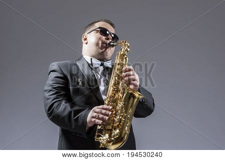 Music Concepts. Portrait of Mature Expressive Caucasian Saxophone Player in Sunglasses Playing the Saxophone in Studio Environment.Horizontal Image Composition