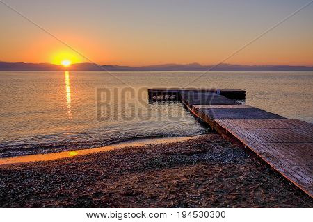 View on the sunrise on the sea the mountains and a wooden pier on the beach Moraitika island Corfu Greece.