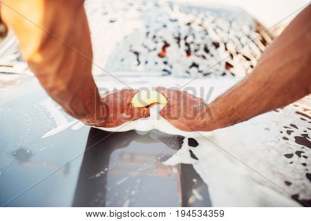 Male hand rubbing the car with foam, carwash