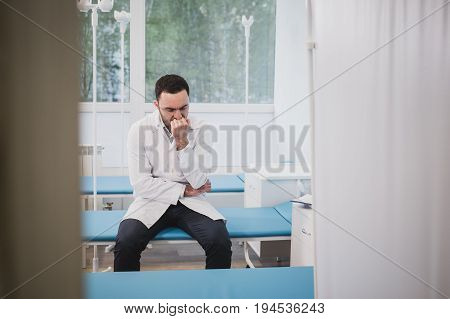 Thoughtful doctor sitting in a operating room with his hand on head.